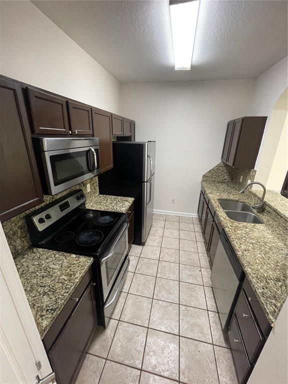 A galley kitchen features dark wood cabinets, granite countertops, and stainless steel appliances — 13536 TURTLE MARSH LOOP UNIT 512, ORLANDO, FL