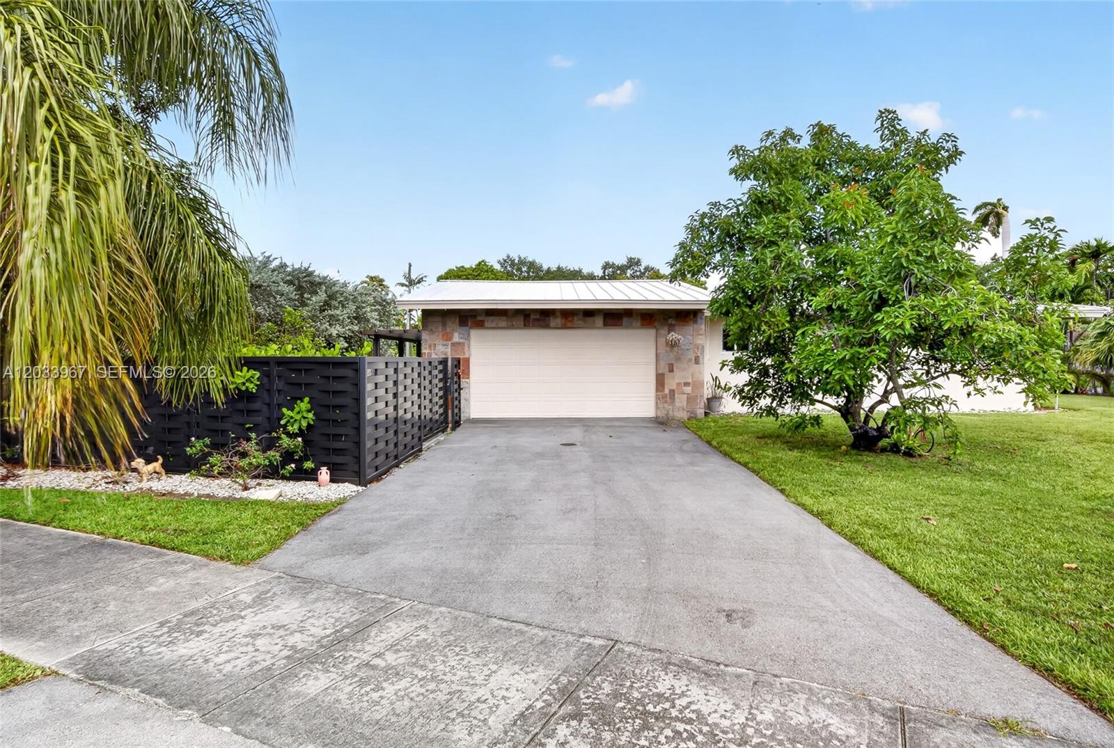 A concrete driveway leads to a single-car garage with stone siding and a metal roof — 8250 SW 118th Ter, Miami FL 33156, MIAMI, FL