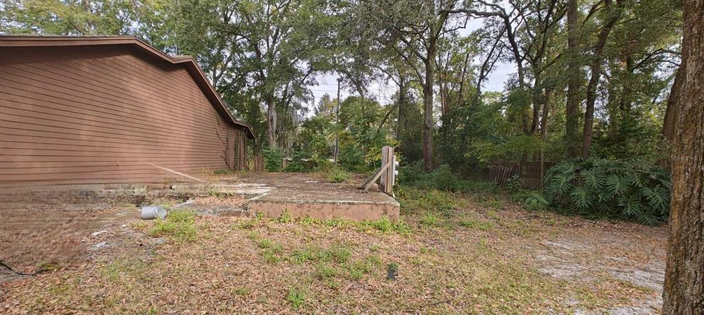 A brown house exterior sits next to a concrete patio slab in a wooded yard — 7520 COLONY COVE LANE, JACKSONVILLE, FL