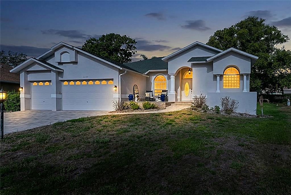 A single-story house with a two-car garage and arched windows at dusk — 2047 OVERBROOK LANE, SPRING HILL, FL