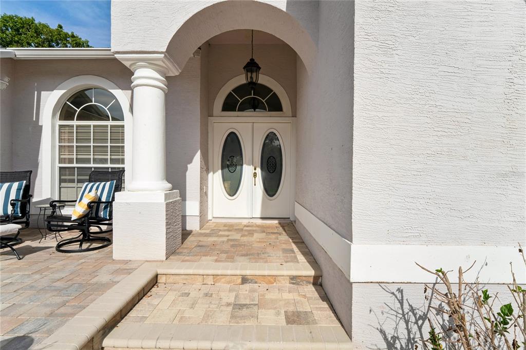 A white arched entryway features double doors with oval glass inserts and a paved porch — 2047 OVERBROOK LANE, SPRING HILL, FL