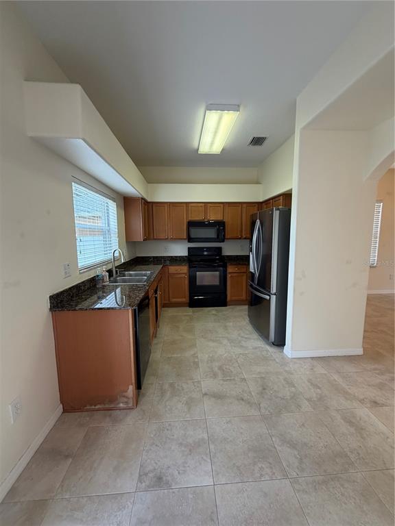 A kitchen features wood cabinets, granite countertops, stainless steel appliances, and light-colored tile flooring — 31037 BACLAN DRIVE, WESLEY CHAPEL, FL