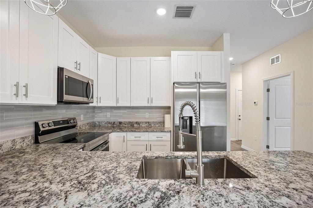 A kitchen features white cabinets, granite countertops, stainless steel appliances, and a double-basin sink — 321 CAMILLIA LANE, PORT CHARLOTTE, FL