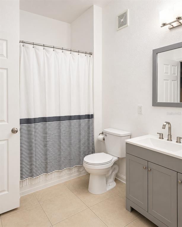A bathroom features a gray vanity, a white toilet, and a shower with a striped curtain — 3314 ROBERT TRENT JONES DRIVE UNIT 10401, ORLANDO, FL