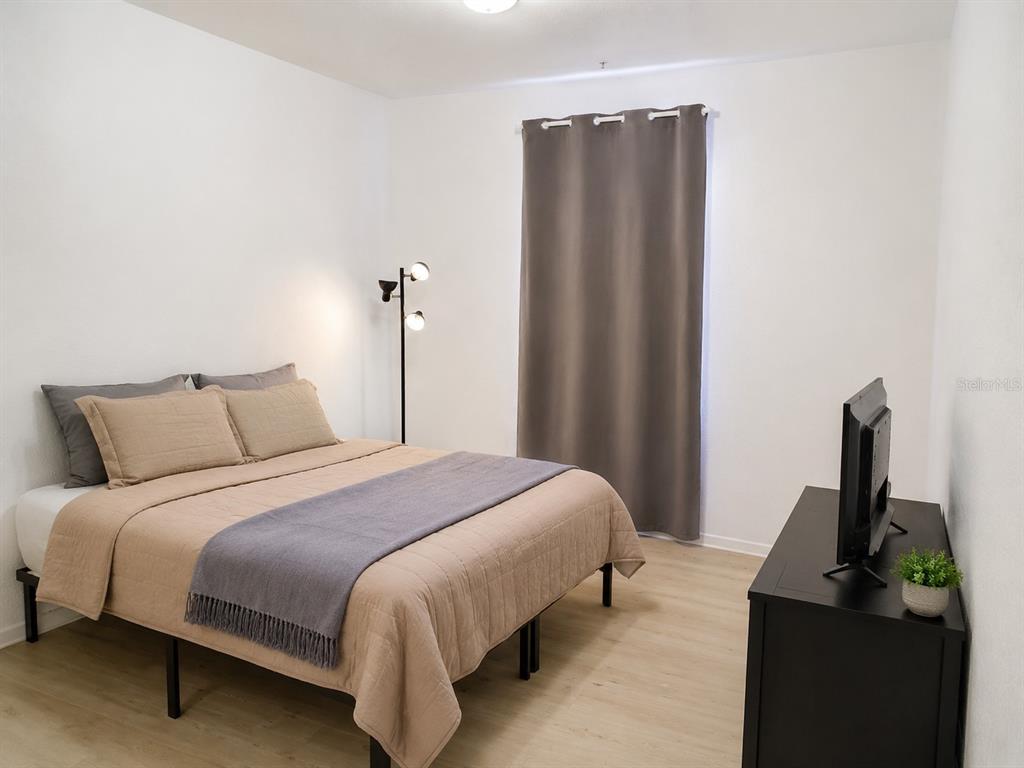 A bedroom features a bed with tan bedding, a floor lamp, and a black television stand — 3314 ROBERT TRENT JONES DRIVE UNIT 10401, ORLANDO, FL