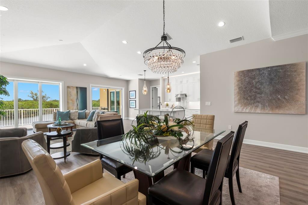 An open-concept dining and living area features a glass-top table, crystal chandelier, and balcony view — 47A BAYVIEW COURT S, ST PETERSBURG, FL