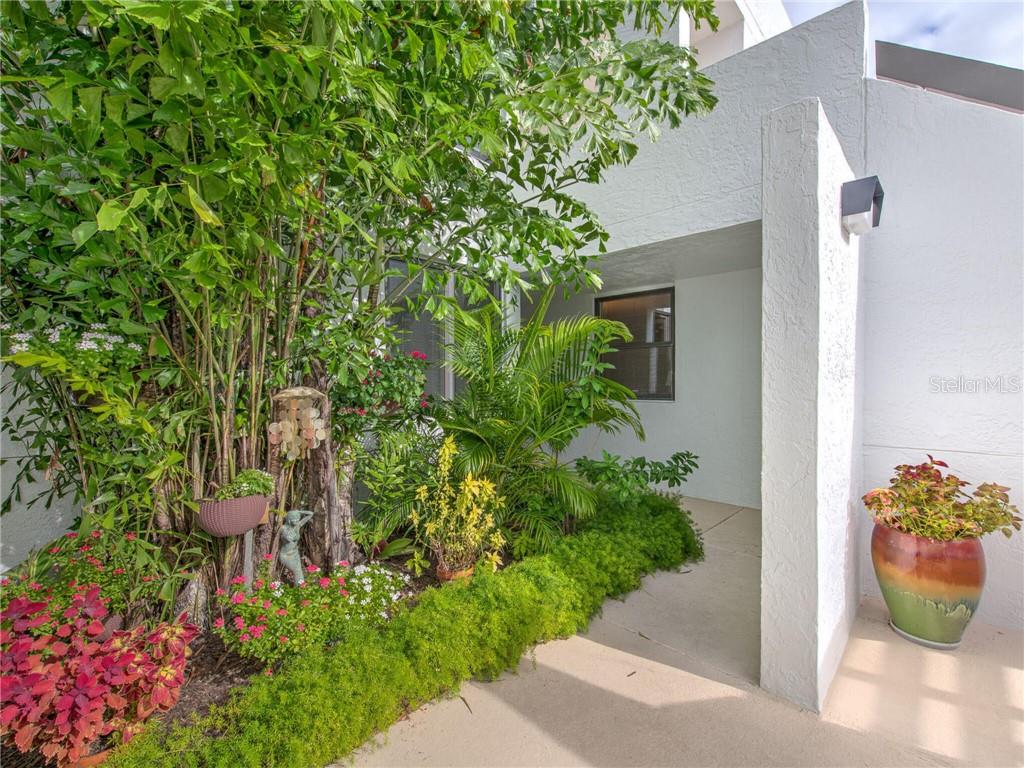 A concrete walkway leads to a home entrance surrounded by lush landscaping and potted plants — 830 BAYPORT WAY UNIT 830, LONGBOAT KEY, FL