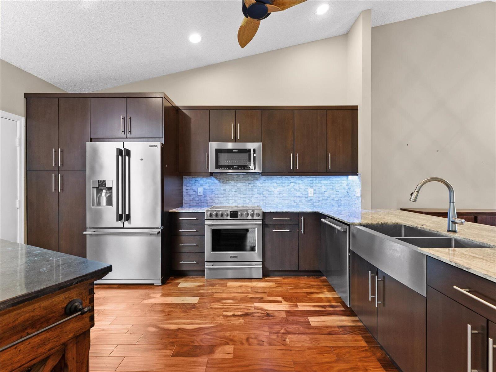 A kitchen features dark wood cabinets, stainless steel appliances, a farmhouse sink, and hardwood floors — 7585 Lexington Club Boulevard # B, Delray Beach FL 33446, DELRAY BEACH, FL