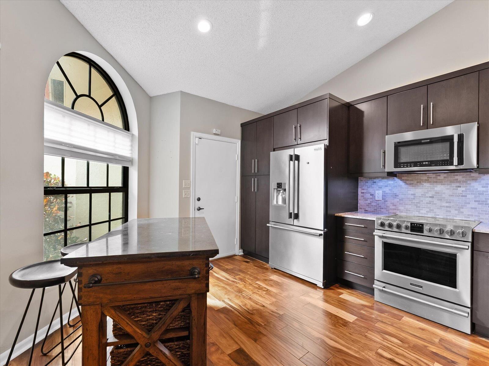 A kitchen with dark wood cabinets, stainless steel appliances, a kitchen island, and arched window — 7585 Lexington Club Boulevard # B, Delray Beach FL 33446, DELRAY BEACH, FL