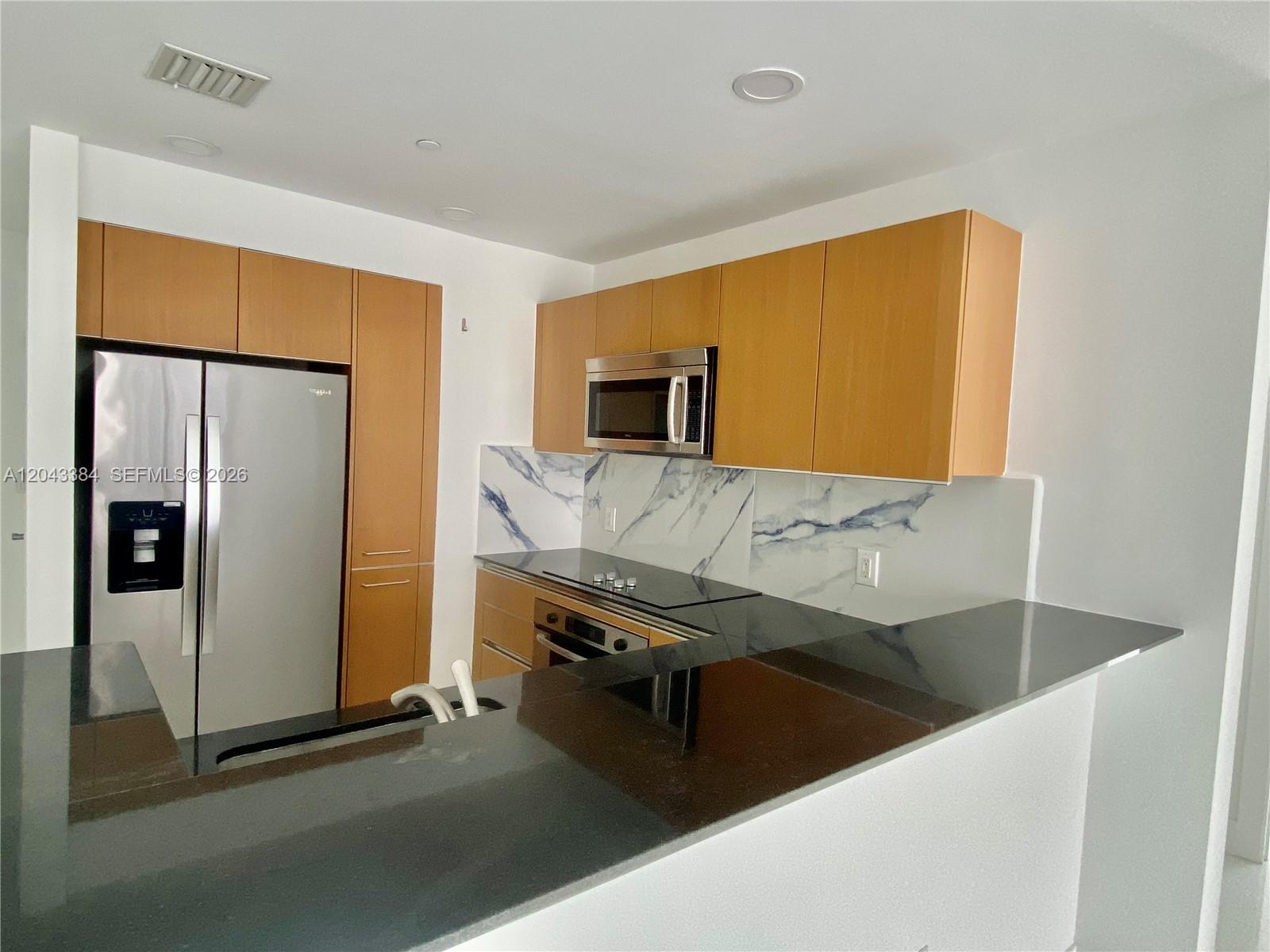 A kitchen features light wood cabinets, black countertops, and a blue-veined marble backsplash — 1060 Brickell Ave # 2911, Miami FL 33131, MIAMI, FL
