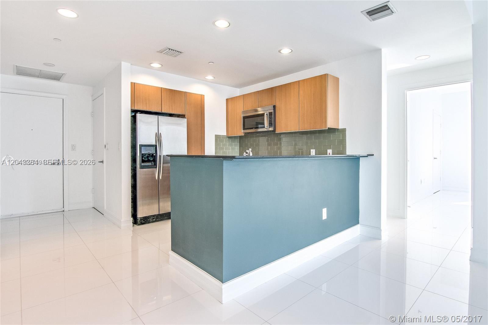 A kitchen features a black granite breakfast bar, stainless steel refrigerator, and wood-toned cabinetry — 1060 Brickell Ave # 2911, Miami FL 33131, MIAMI, FL