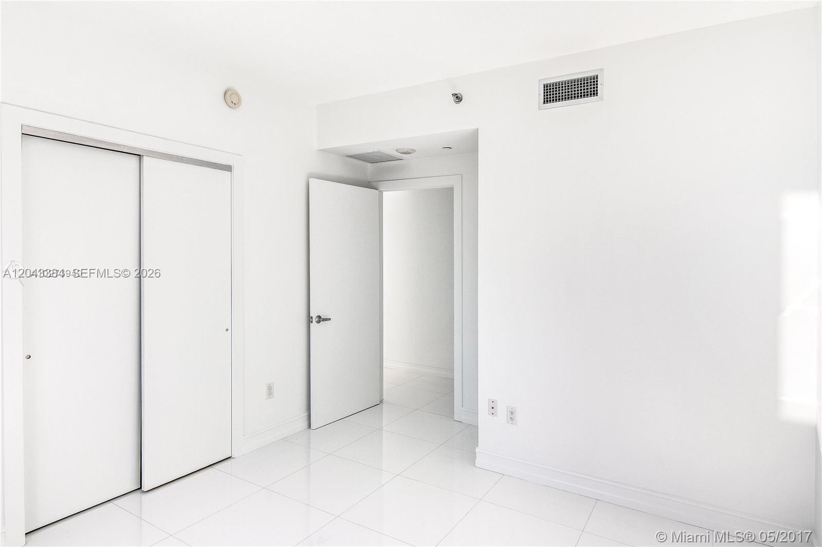 An empty room features white tile floors, white walls, and floor-to-ceiling windows overlooking buildings — 1060 Brickell Ave # 2911, Miami FL 33131, MIAMI, FL