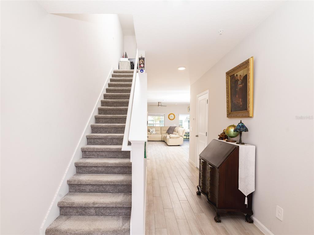 A carpeted staircase leads upstairs next to a hallway with tile flooring and furniture — 152 CAPE HONEYSUCKLE PLACE, SANFORD, FL