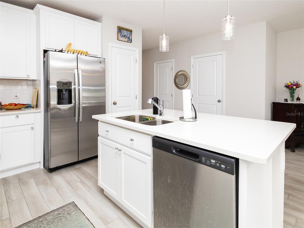 A kitchen features white cabinets, stainless steel appliances, a center island, and light wood flooring — 152 CAPE HONEYSUCKLE PLACE, SANFORD, FL