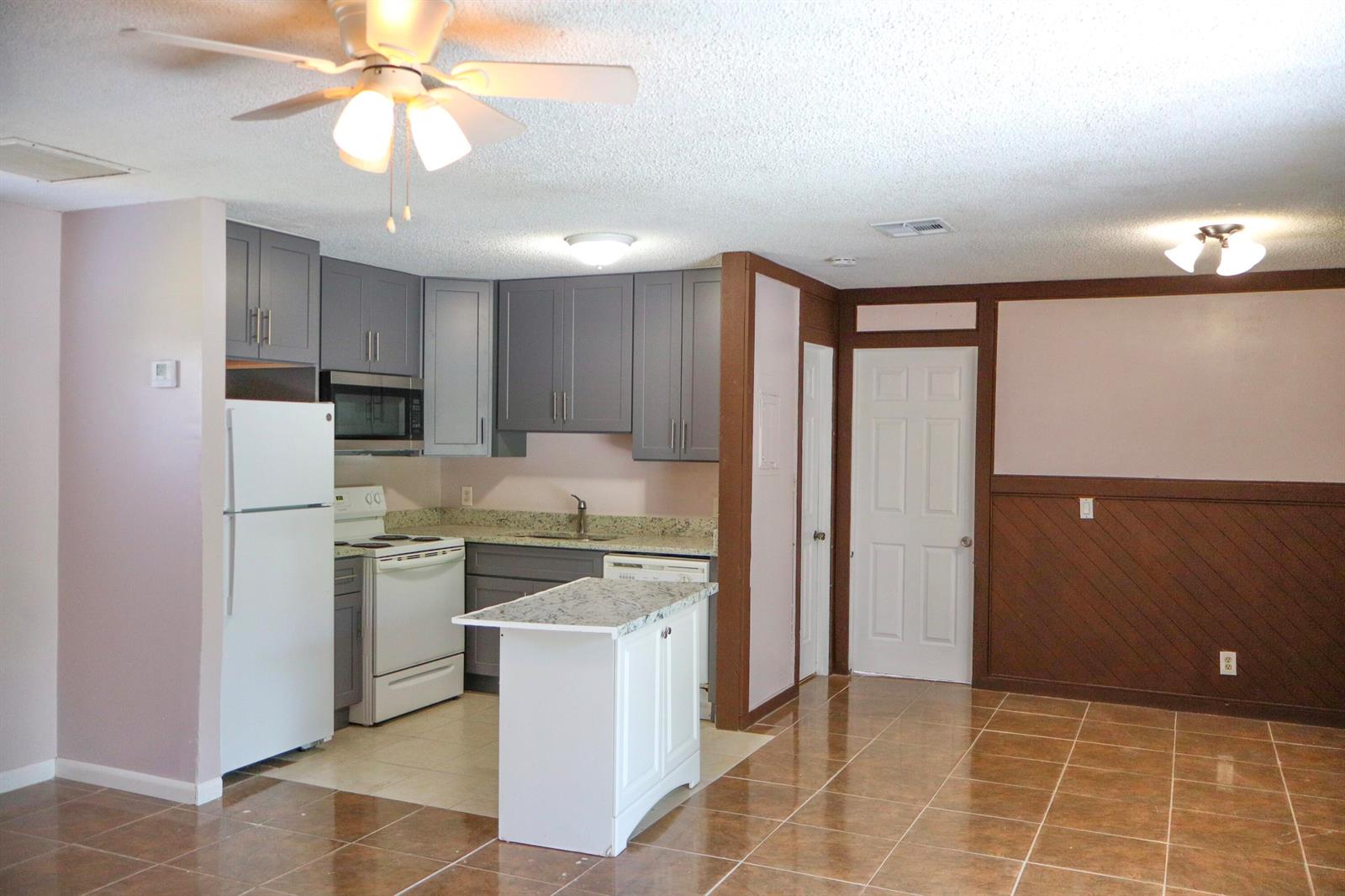 A kitchen with gray cabinets, white appliances, and a small island sits beside a dining area — 34 Crossings Circle # F, Boynton Beach FL 33435, BOYNTON BEACH, FL