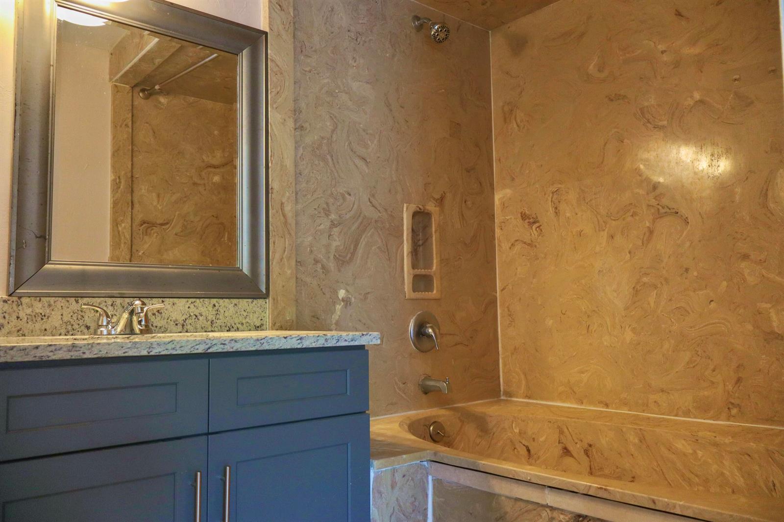 A bathroom features a blue vanity with a granite countertop and a marble-tiled tub surround — 34 Crossings Circle # F, Boynton Beach FL 33435, BOYNTON BEACH, FL