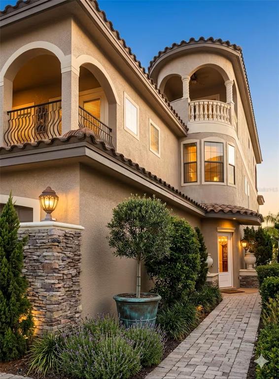 A multi-story stucco house features a stone pillar, arched balconies, and a paved walkway — 841 DESERT MOUNTAIN COURT, REUNION, FL