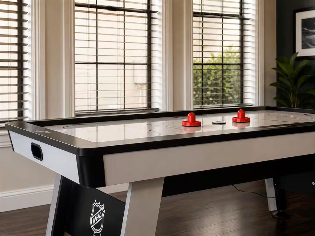 An air hockey table sits in a room with large windows and dark wood flooring — 841 DESERT MOUNTAIN COURT, REUNION, FL
