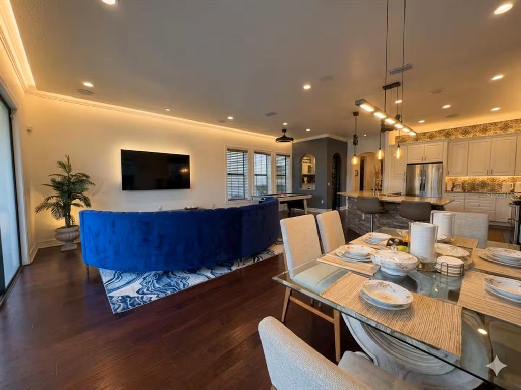 An open-concept living and dining area features a blue curved sofa, hardwood floors, and kitchen — 841 DESERT MOUNTAIN COURT, REUNION, FL