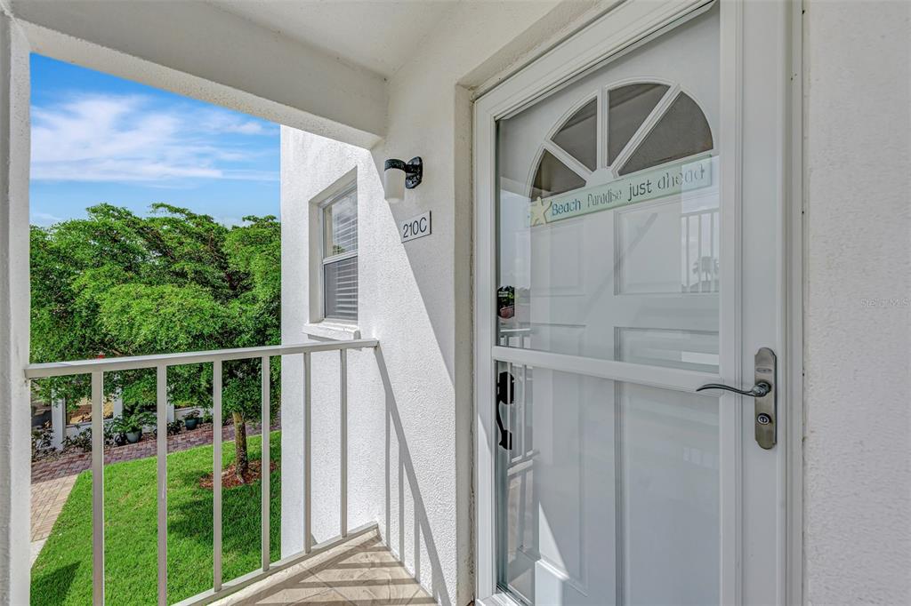 A white door with a glass insert and a balcony railing overlooking a grassy area — 116 VISTA HERMOSA CIRCLE UNIT 210C, SARASOTA, FL