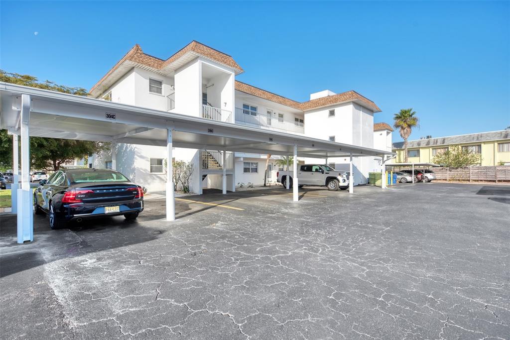 A multi-story apartment building features a covered parking area with several parked vehicles — 116 VISTA HERMOSA CIRCLE UNIT 210C, SARASOTA, FL