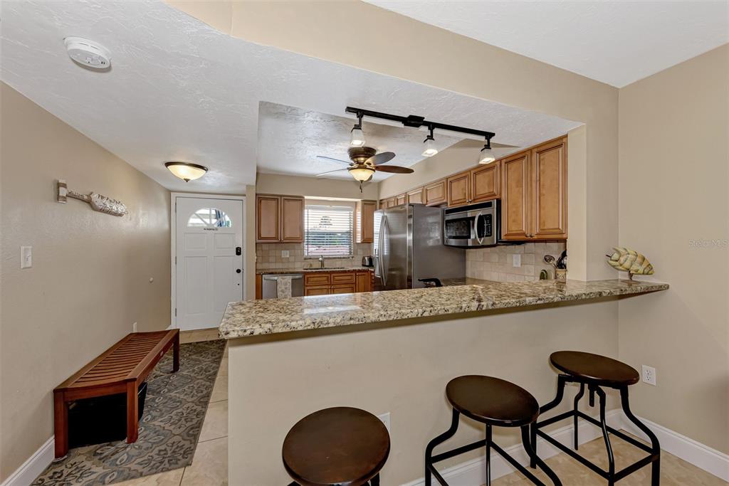 A kitchen with granite countertops, wooden cabinets, and a breakfast bar with three stools — 116 VISTA HERMOSA CIRCLE UNIT 210C, SARASOTA, FL