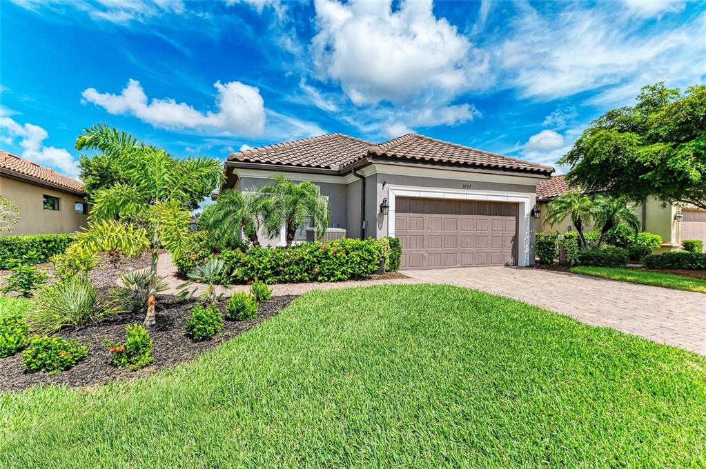 A single-story house with a tiled roof, a two-car garage, and a landscaped front yard — 8737 BELLUSSI DRIVE, SARASOTA, FL
