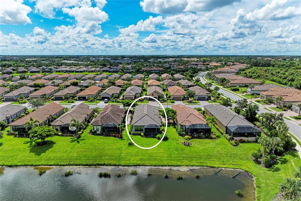 An aerial view shows a residential house with a screened-in patio overlooking a pond — 8737 BELLUSSI DRIVE, SARASOTA, FL
