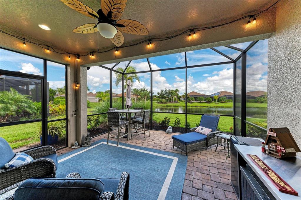 A screened-in patio features a brick floor, outdoor furniture, a ceiling fan, and lake views — 8737 BELLUSSI DRIVE, SARASOTA, FL