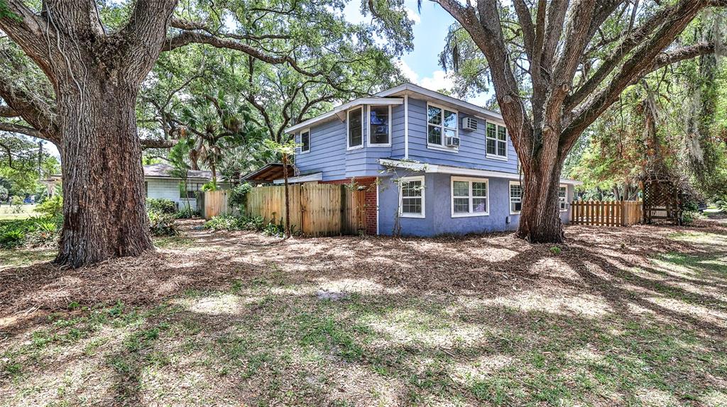 A two-story blue house with a wooden fence sits among large trees in a yard — 801 E 20TH STREET, SANFORD, FL