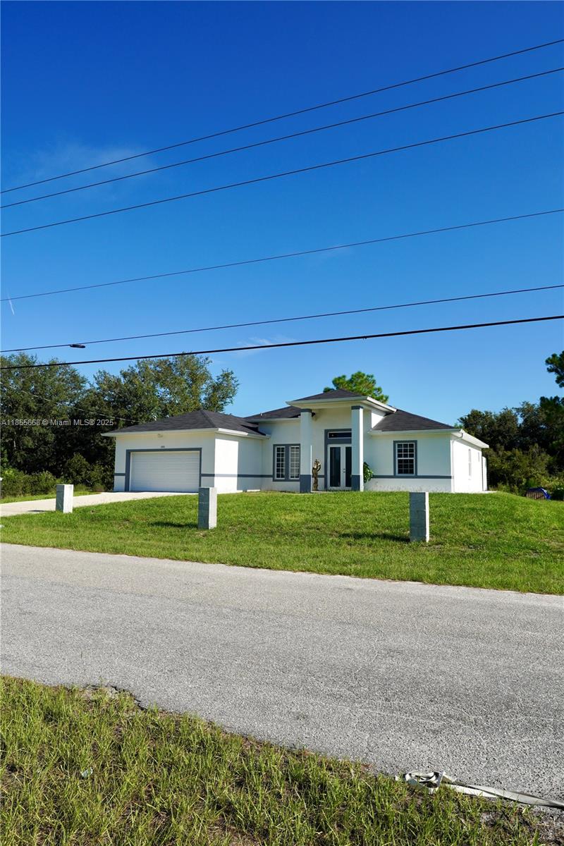 A single-story white house with a garage and a covered entryway sits on a lawn — 105 E 15th st, Lehigh Acres FL 33972, LEHIGH ACRES, FL
