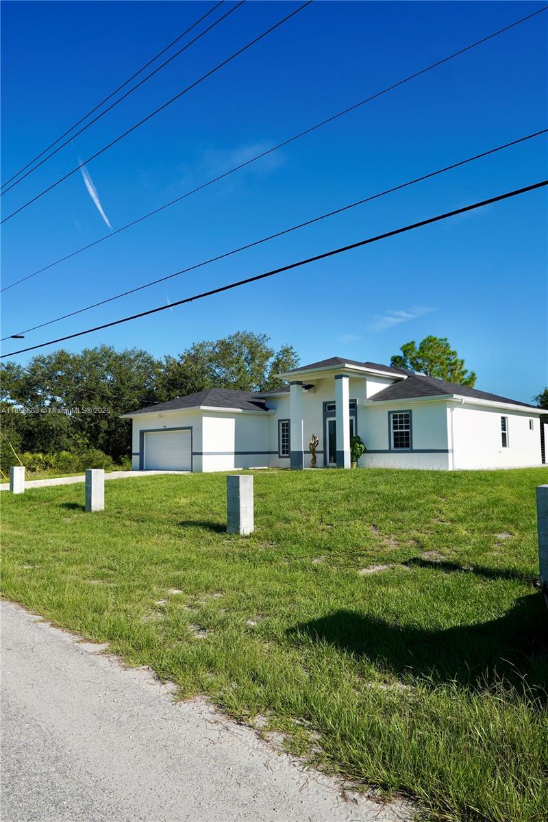 A single-story white house with a dark roof and a garage sits on a grassy lot — 105 E 15th st, Lehigh Acres FL 33972, LEHIGH ACRES, FL