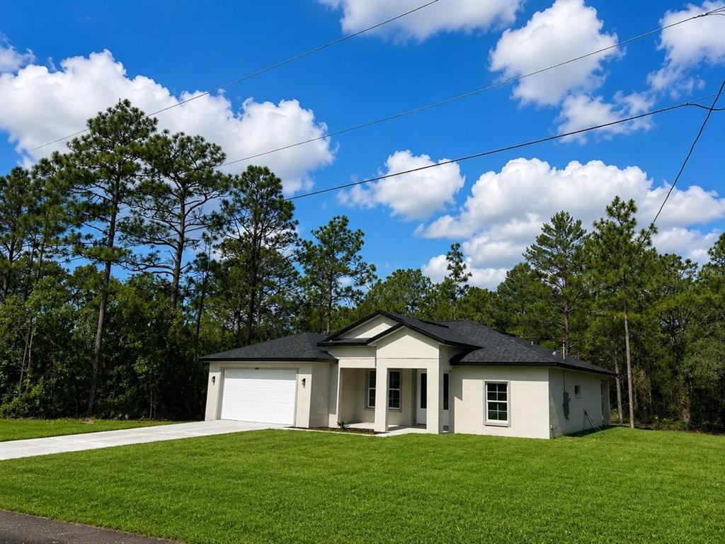 A single-story house with a white stucco exterior, dark roof, and attached garage — 6476 N SANDBORN LOOP, DUNNELLON, FL