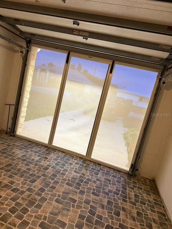 A garage with tiled flooring and a glass-paneled door looking out onto a driveway — 4418 SW 1ST AVENUE, CAPE CORAL, FL