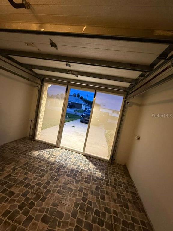 A garage with tiled flooring and a sliding glass door looking out onto a driveway — 4418 SW 1ST AVENUE, CAPE CORAL, FL