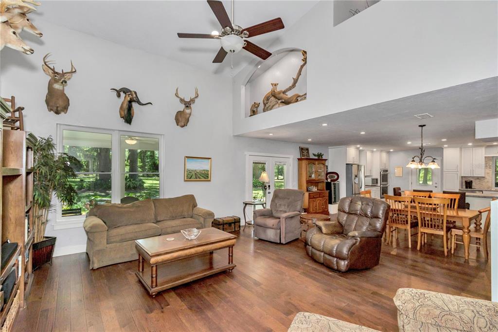 A living room with vaulted ceilings, taxidermy, hardwood floors, and an open dining area — 26354 NW 94TH AVENUE, HIGH SPRINGS, FL