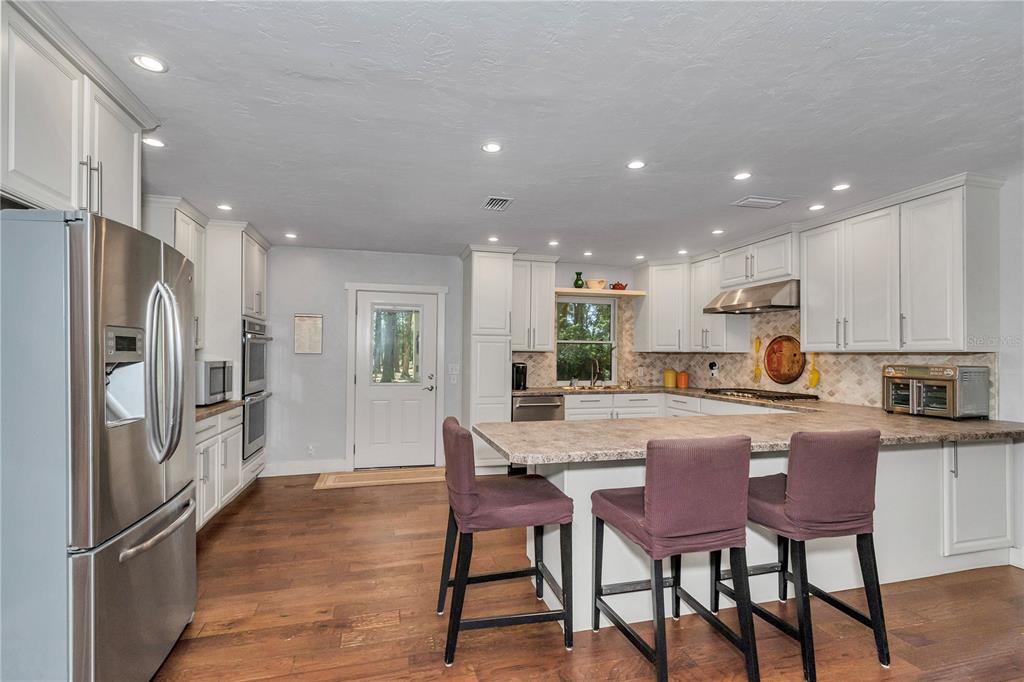 A kitchen features white cabinetry, stainless steel appliances, a center island, and wood flooring — 26354 NW 94TH AVENUE, HIGH SPRINGS, FL