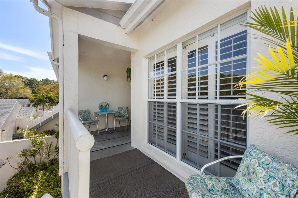 A covered balcony features a small table with two chairs and a view of trees — 11600 SHIPWATCH DRIVE UNIT 1417, LARGO, FL