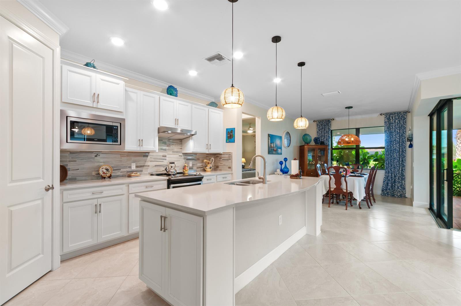 A white kitchen features a large island, pendant lighting, and an adjacent dining area — 5947 Prosperity Lane, Ave Maria FL 34142, AVE MARIA, FL