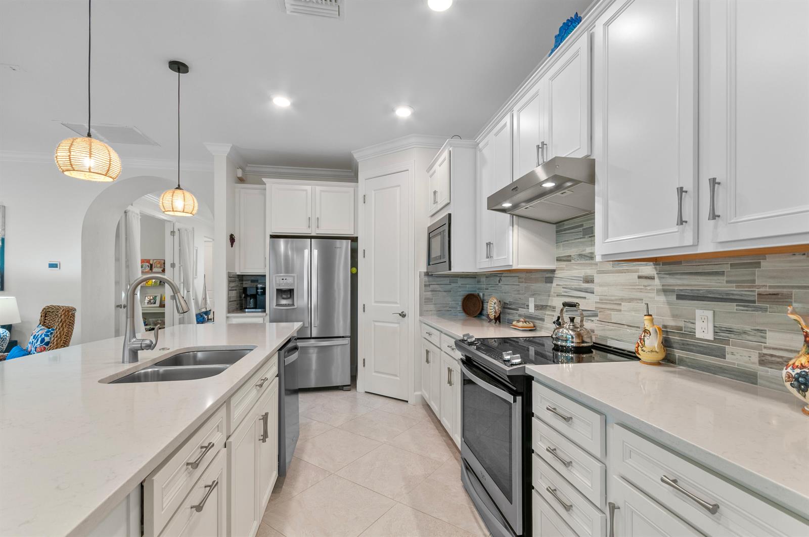 A modern kitchen features white cabinetry, stainless steel appliances, a quartz island, and tile backsplash — 5947 Prosperity Lane, Ave Maria FL 34142, AVE MARIA, FL