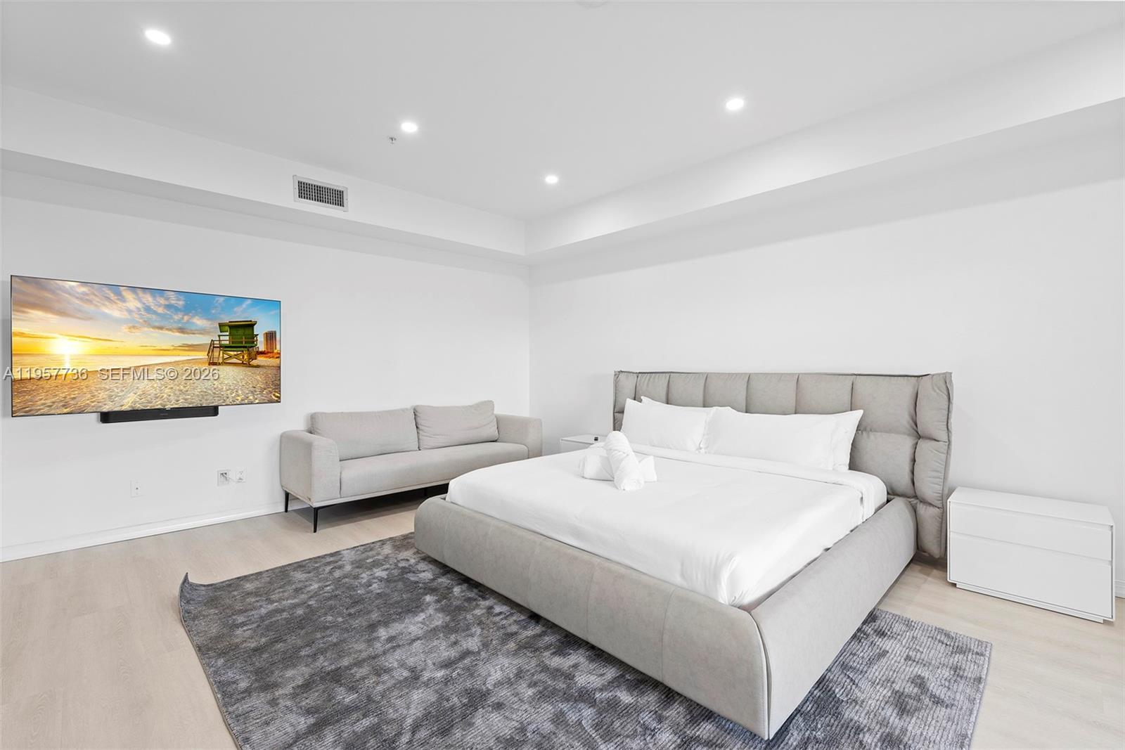 A modern bedroom features a gray upholstered bed, a matching sofa, and a wall-mounted television — 1415 Sunset Harbour Dr # 204, Miami Beach FL 33139, MIAMI BEACH, FL