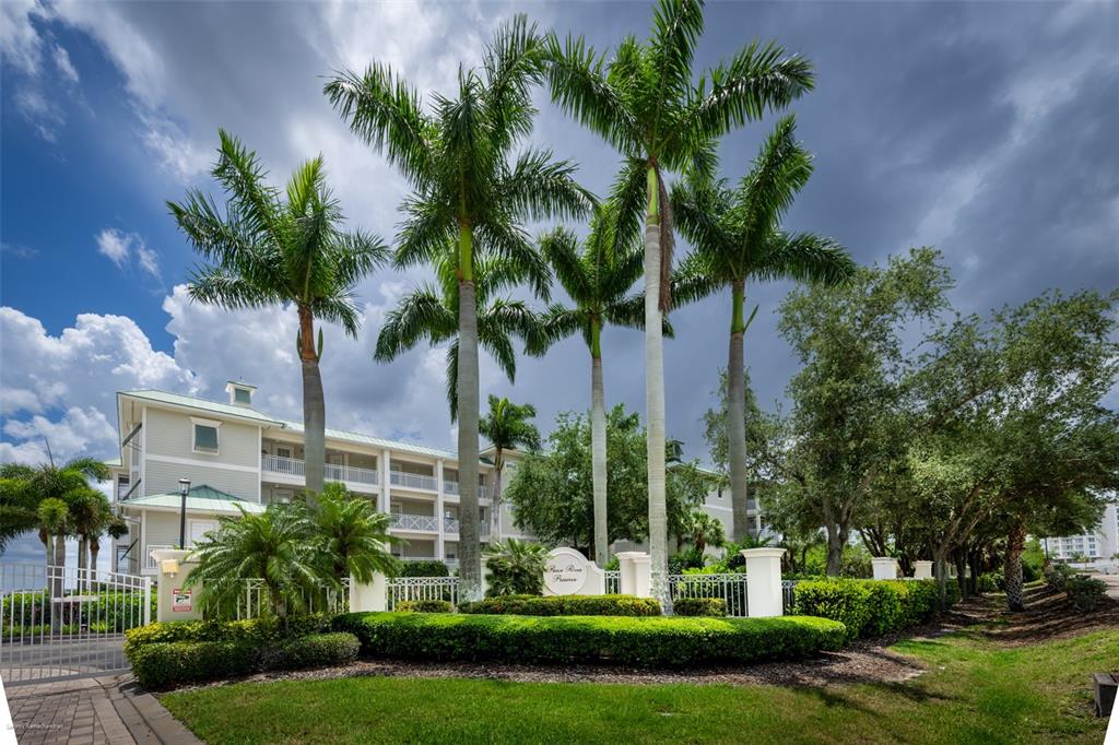 A multi-story apartment building stands behind a landscaped entrance with palm trees and hedges — 5116 MELBOURNE STREET UNIT B303, PUNTA GORDA, FL