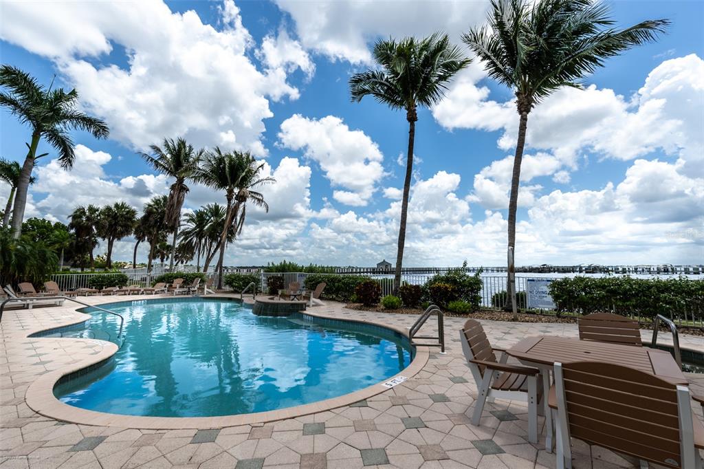 A swimming pool with a patio and palm trees overlooks a bay with a pier — 5116 MELBOURNE STREET UNIT B303, PUNTA GORDA, FL