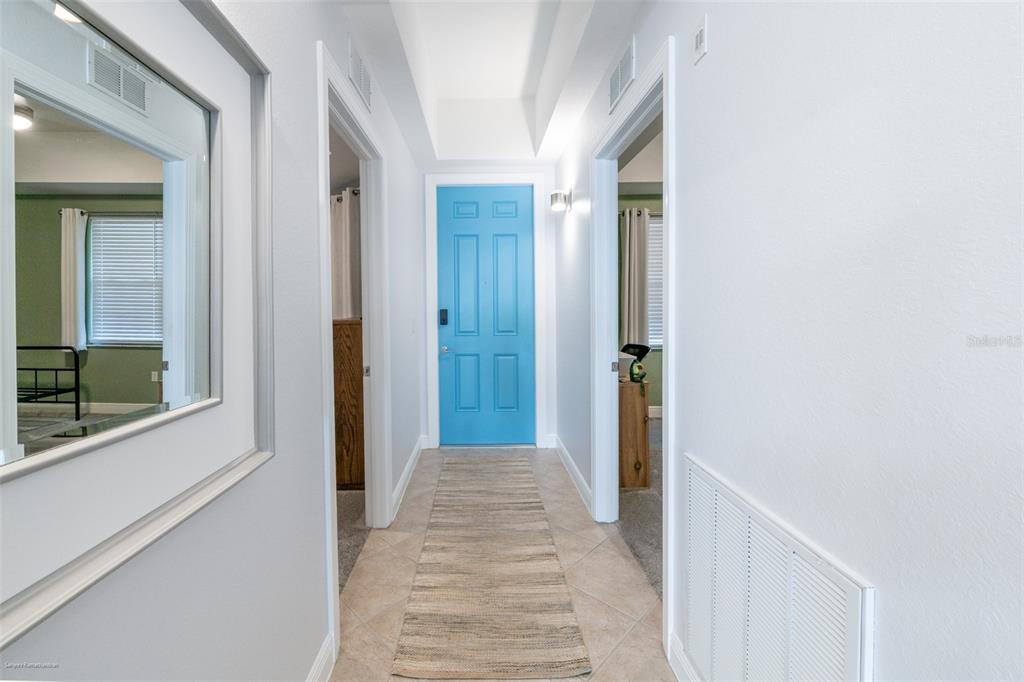 A hallway features a bright blue door, tile flooring, a runner rug, and white walls — 5116 MELBOURNE STREET UNIT B303, PUNTA GORDA, FL