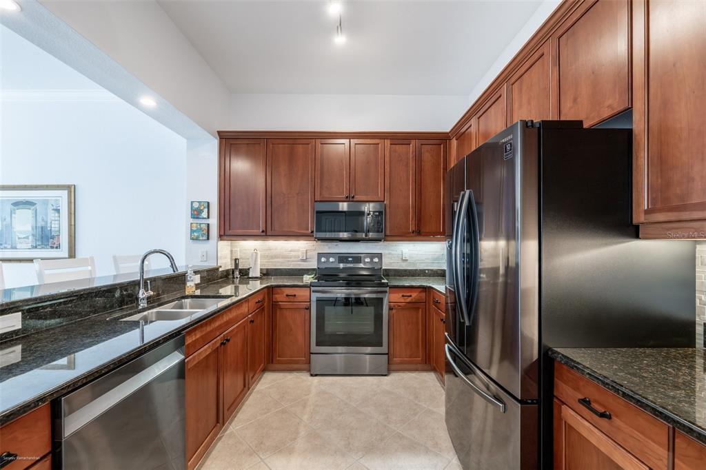 A kitchen features cherry wood cabinets, stainless steel appliances, and dark granite countertops — 5116 MELBOURNE STREET UNIT B303, PUNTA GORDA, FL