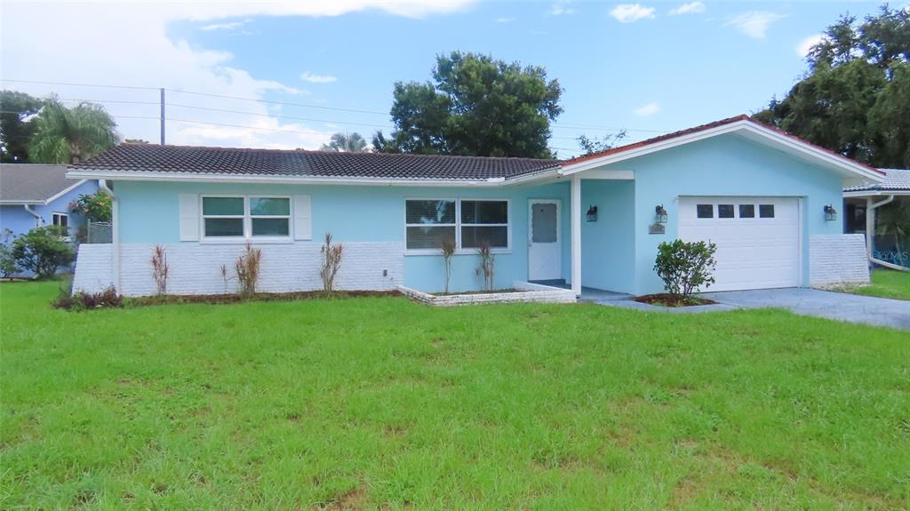 A light blue, single-story ranch-style house features a white garage door and a grassy lawn — 2459 RUTLAND LANE, CLEARWATER, FL