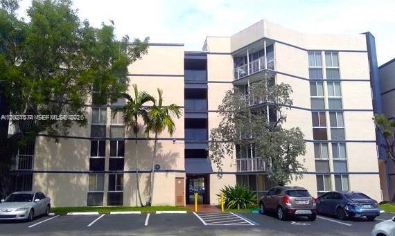 A multi-story apartment building with a parking lot in the foreground and palm trees — 7075 NW 186th St # C207, Hialeah FL 33015, HIALEAH, FL