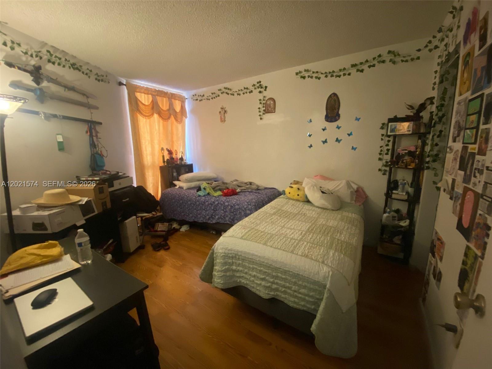 A bedroom with two twin beds, wood flooring, and decorative wall vines and butterflies — 7075 NW 186th St # C207, Hialeah FL 33015, HIALEAH, FL