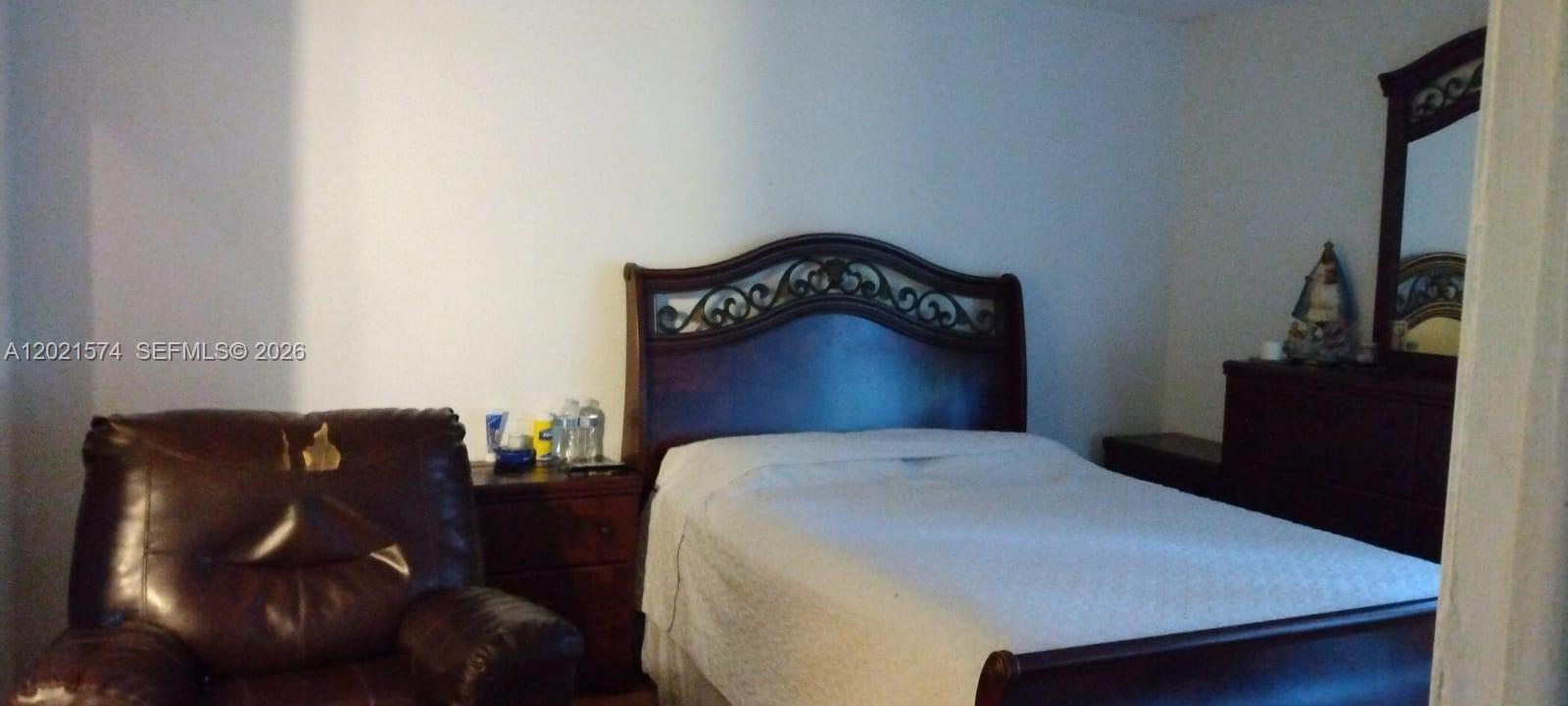 A bedroom features a dark wood bed frame, a matching nightstand, and a brown leather chair — 7075 NW 186th St # C207, Hialeah FL 33015, HIALEAH, FL