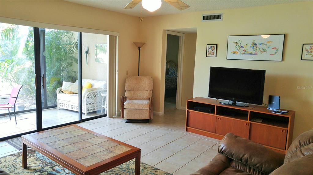 A living room features tile flooring, a television console, a recliner, and a sliding glass door — 5677 ASHTON LAKE DRIVE UNIT 11, SARASOTA, FL